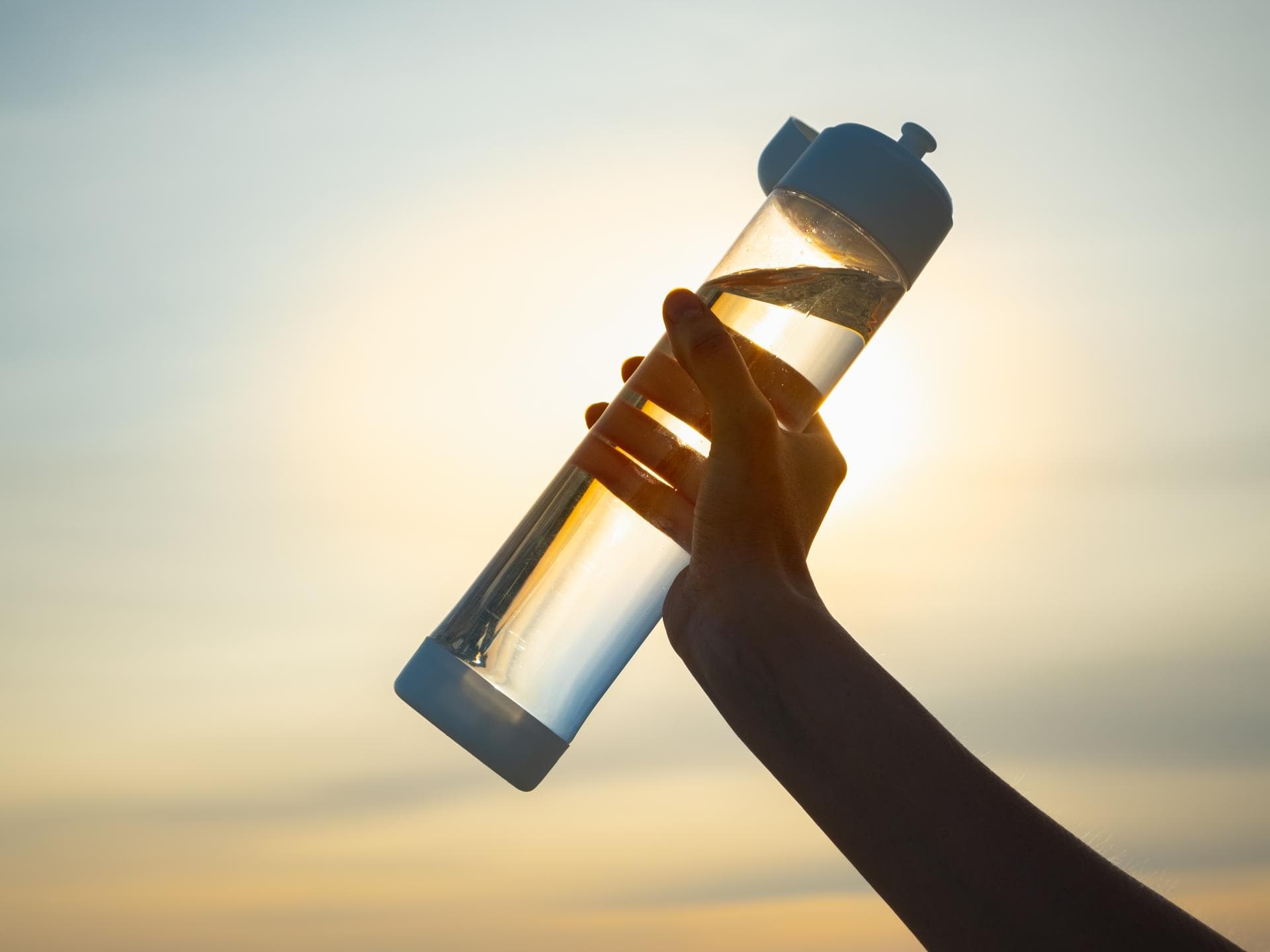 Frau hält Trinkflasche in die abendliche Sonne