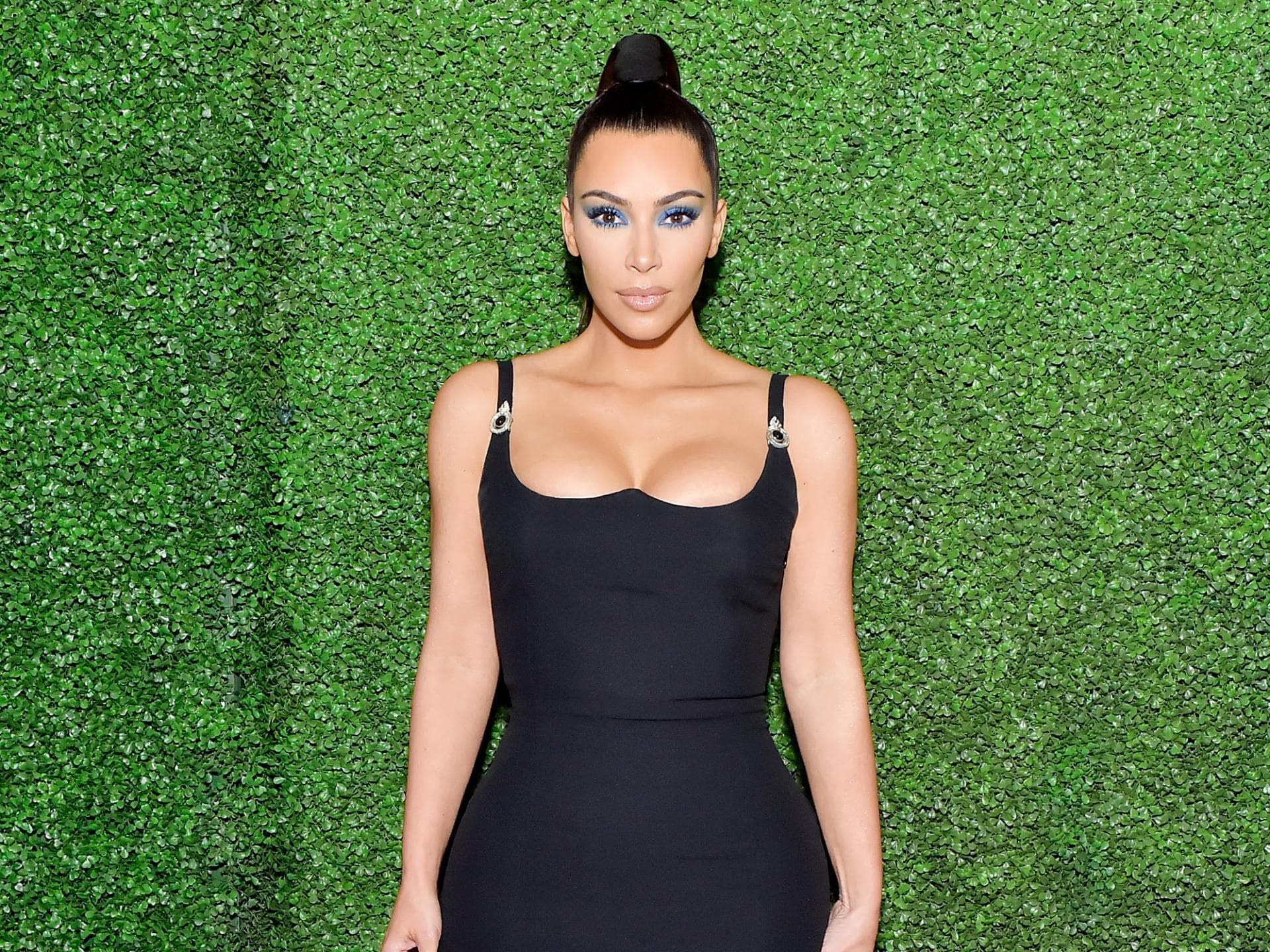 Kim Kardashian im schwarzen Kleid vor grüner Wand