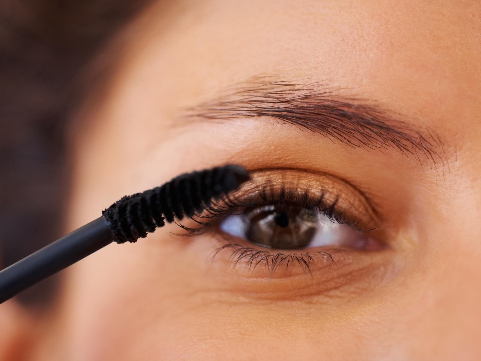 Frau trägt Mascara auf mit braunen Augen