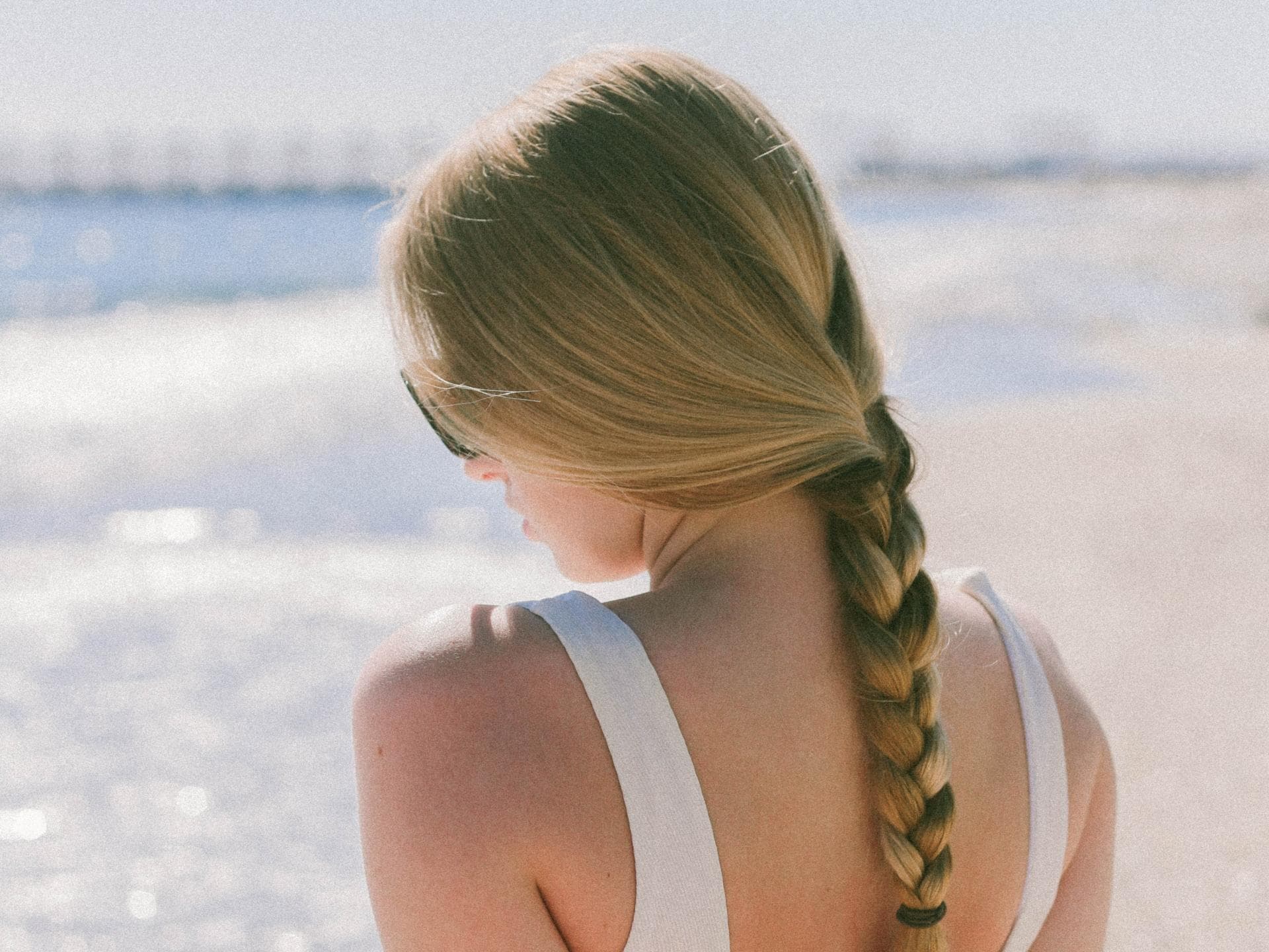 Frau mit geflochtenen Haaren sitzt am Strand