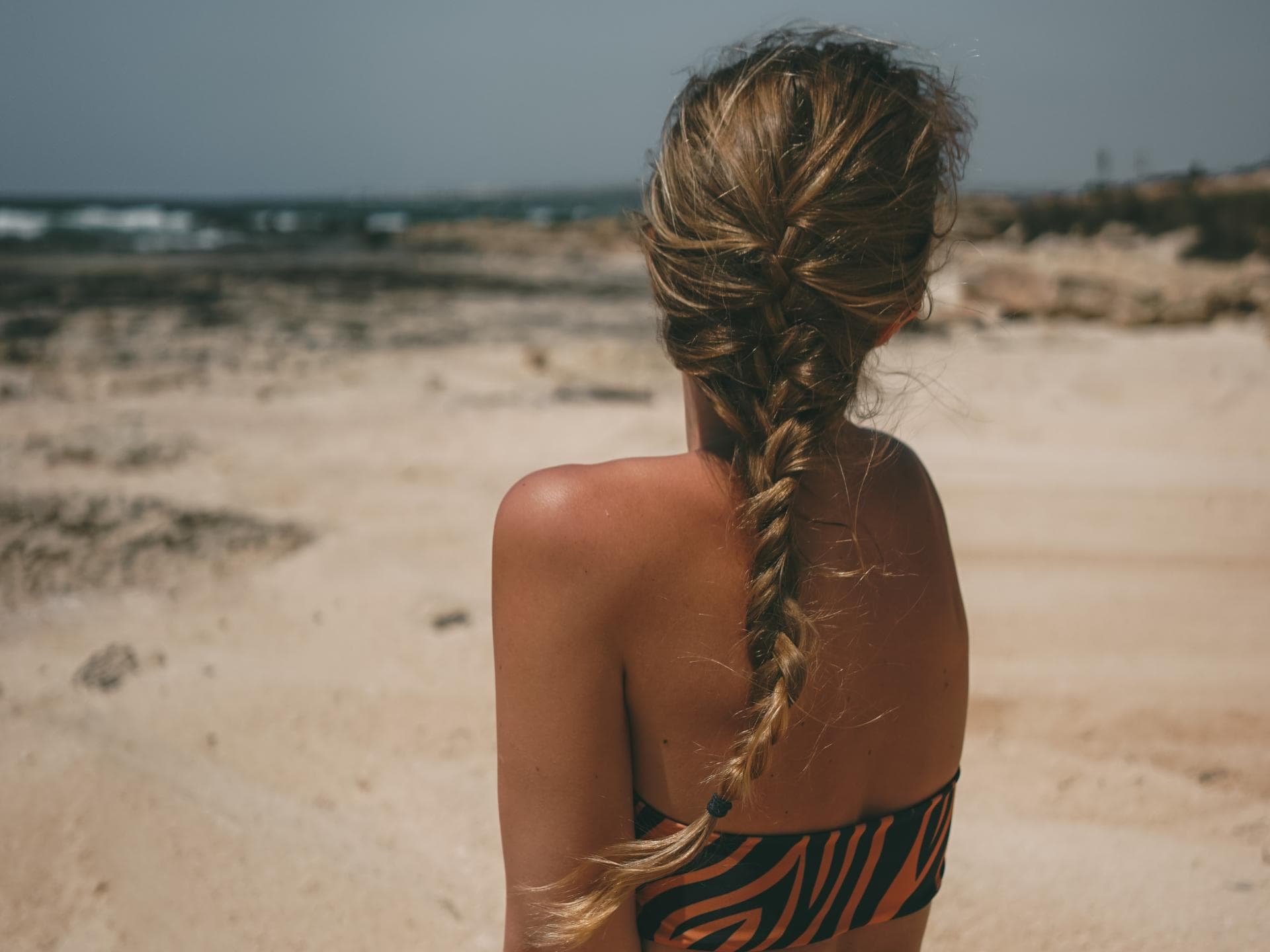 Frau mit geflochtenen Haaren sitzt am Strand