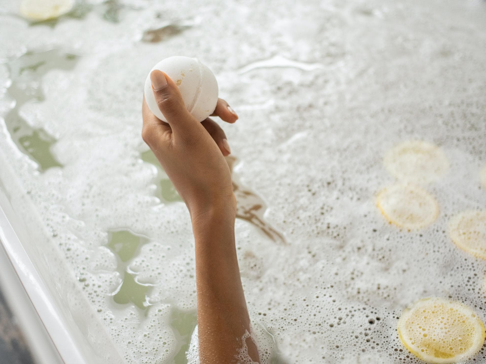 Badekugel in Hand und Badewanne