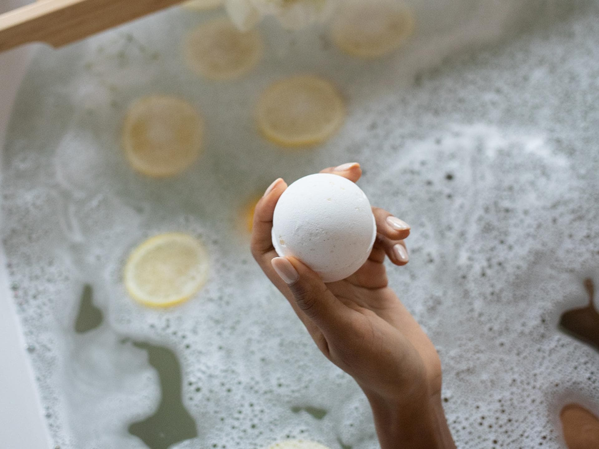 Frau hält Badekugel in der Badewanne