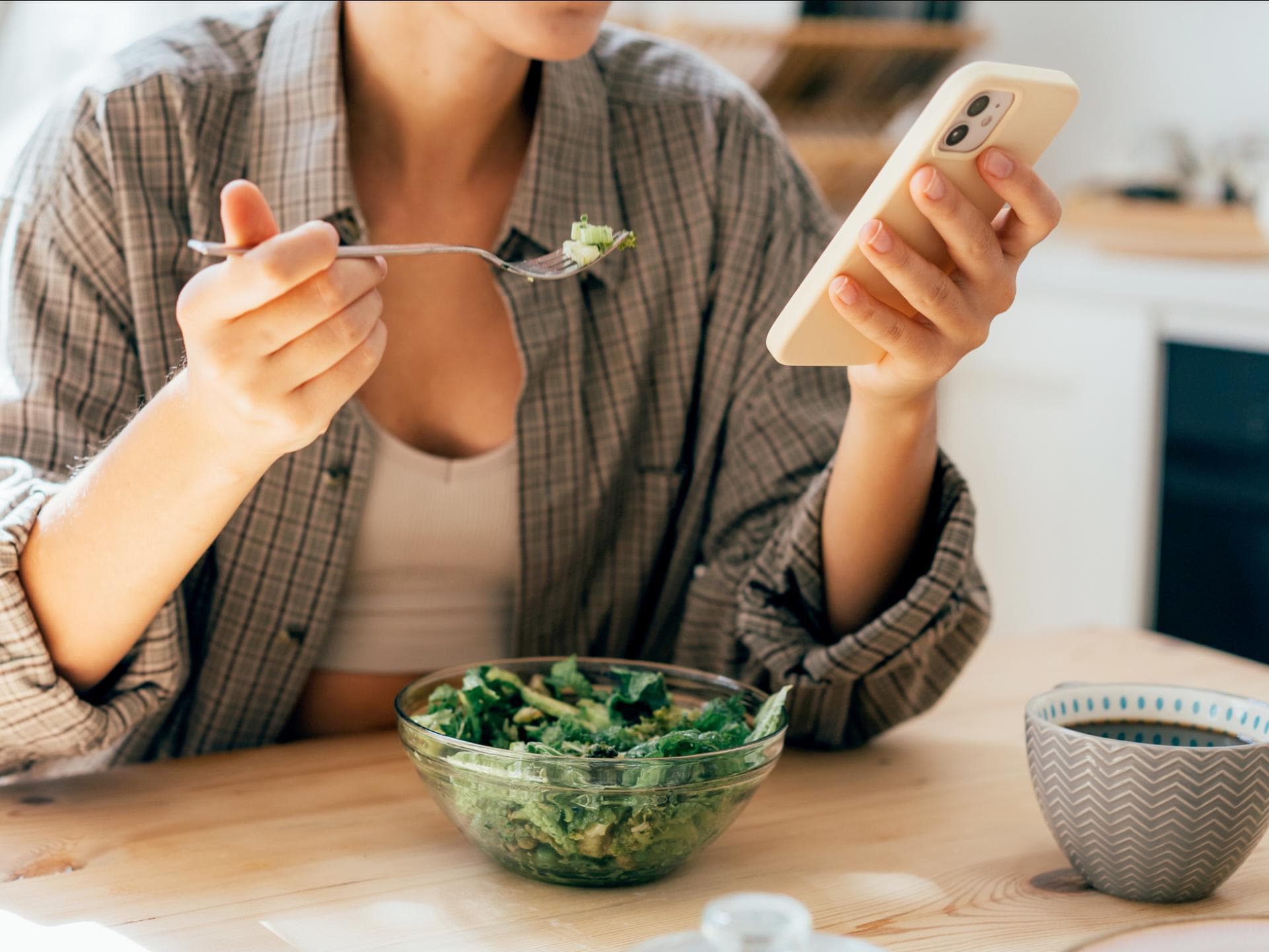 Frau isst Salat mit Smartphone in der Hand