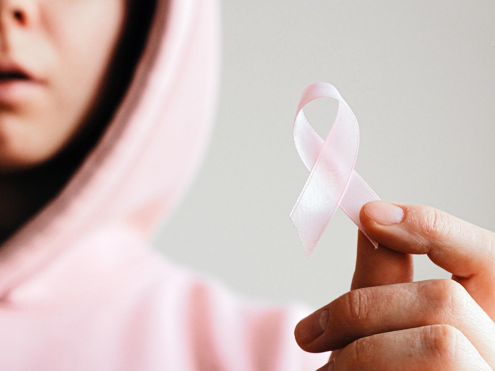Frau mit pinkem Hoodie hält eine pinke Schleife in der Hand