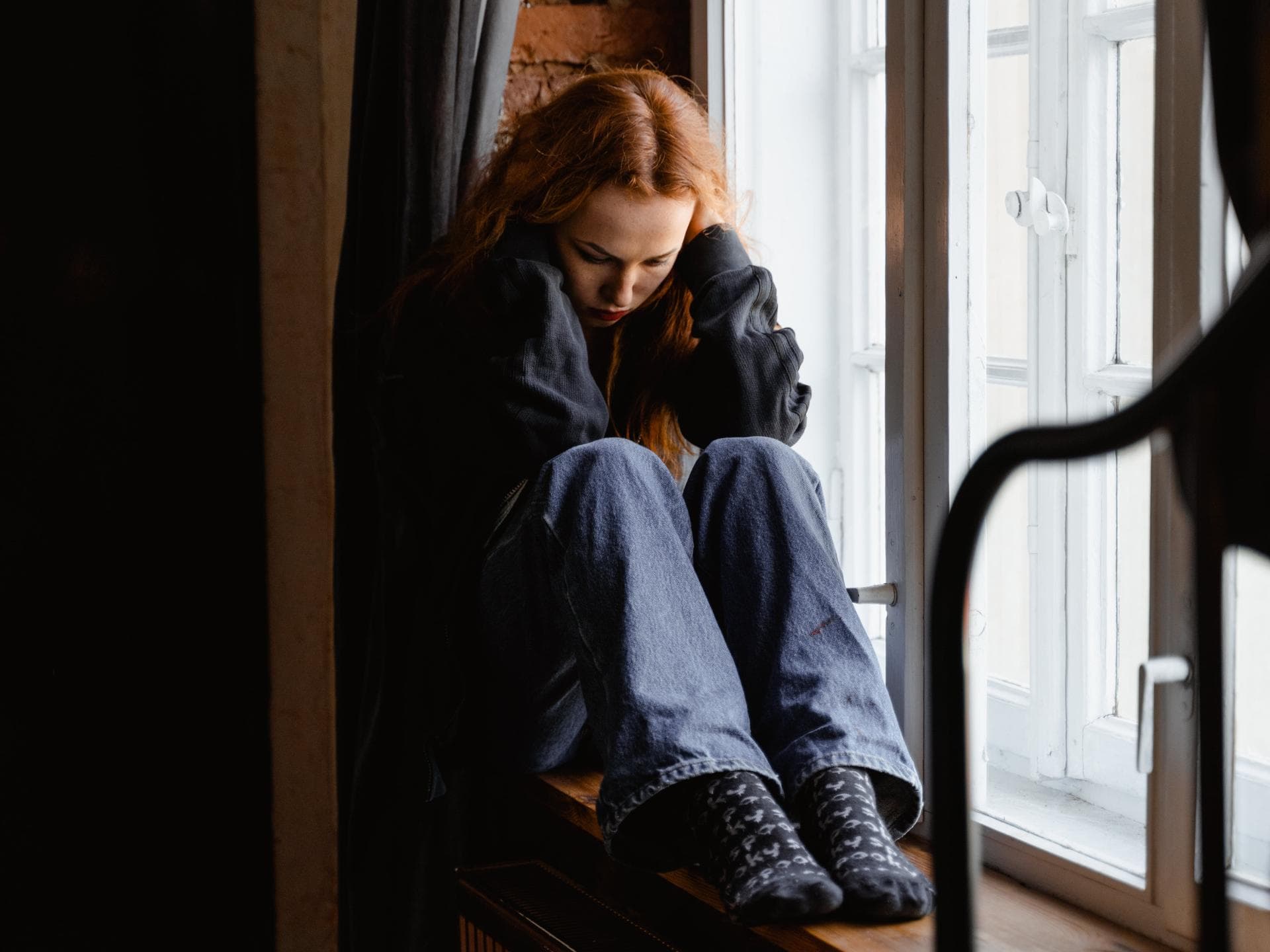 Traurige Frau sitzt auf einer Fensterbank