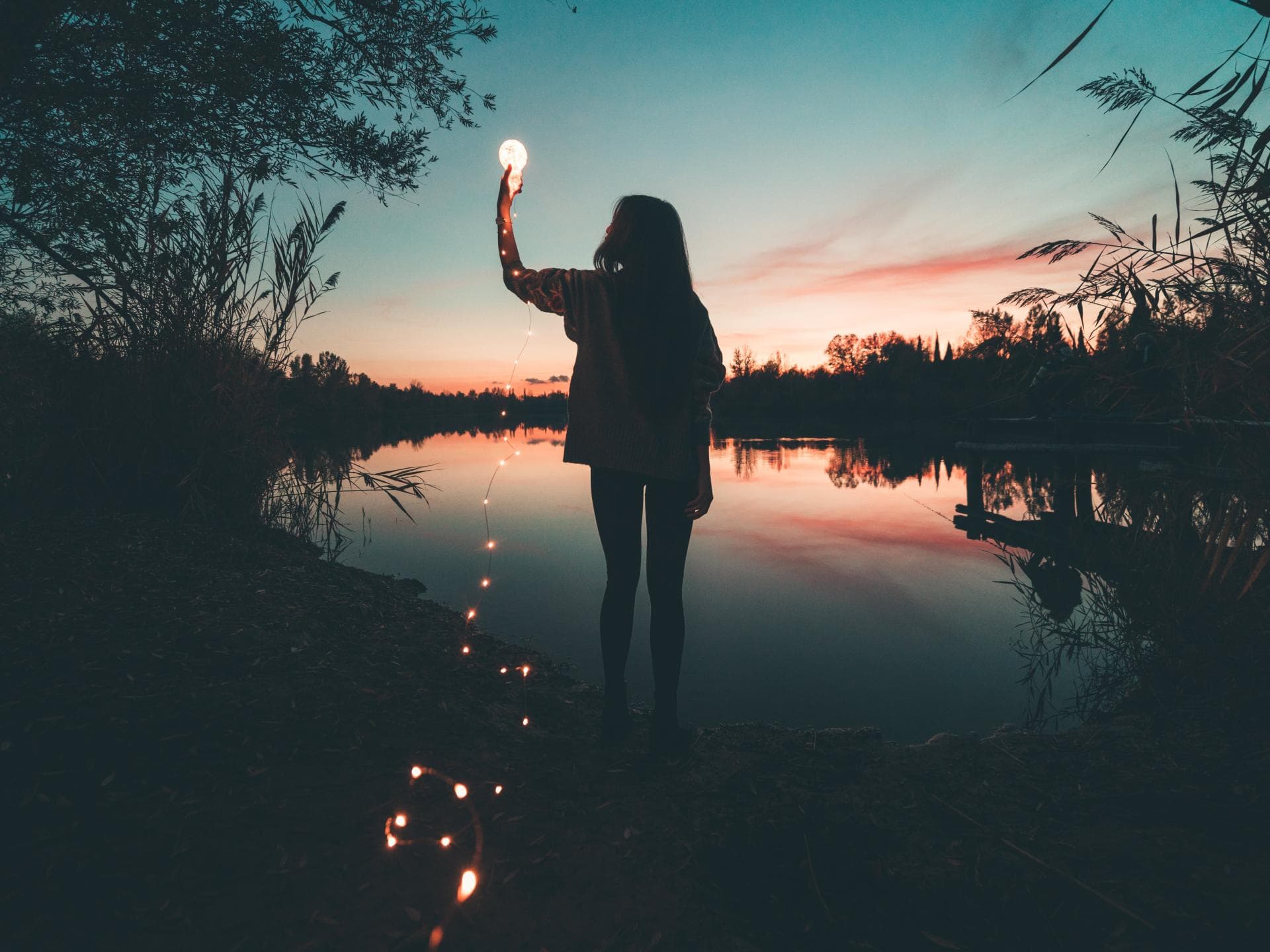 Horoskop Wochenende Frau am See hält eine Glühbirne mit einer Lichterkette in der Hand.