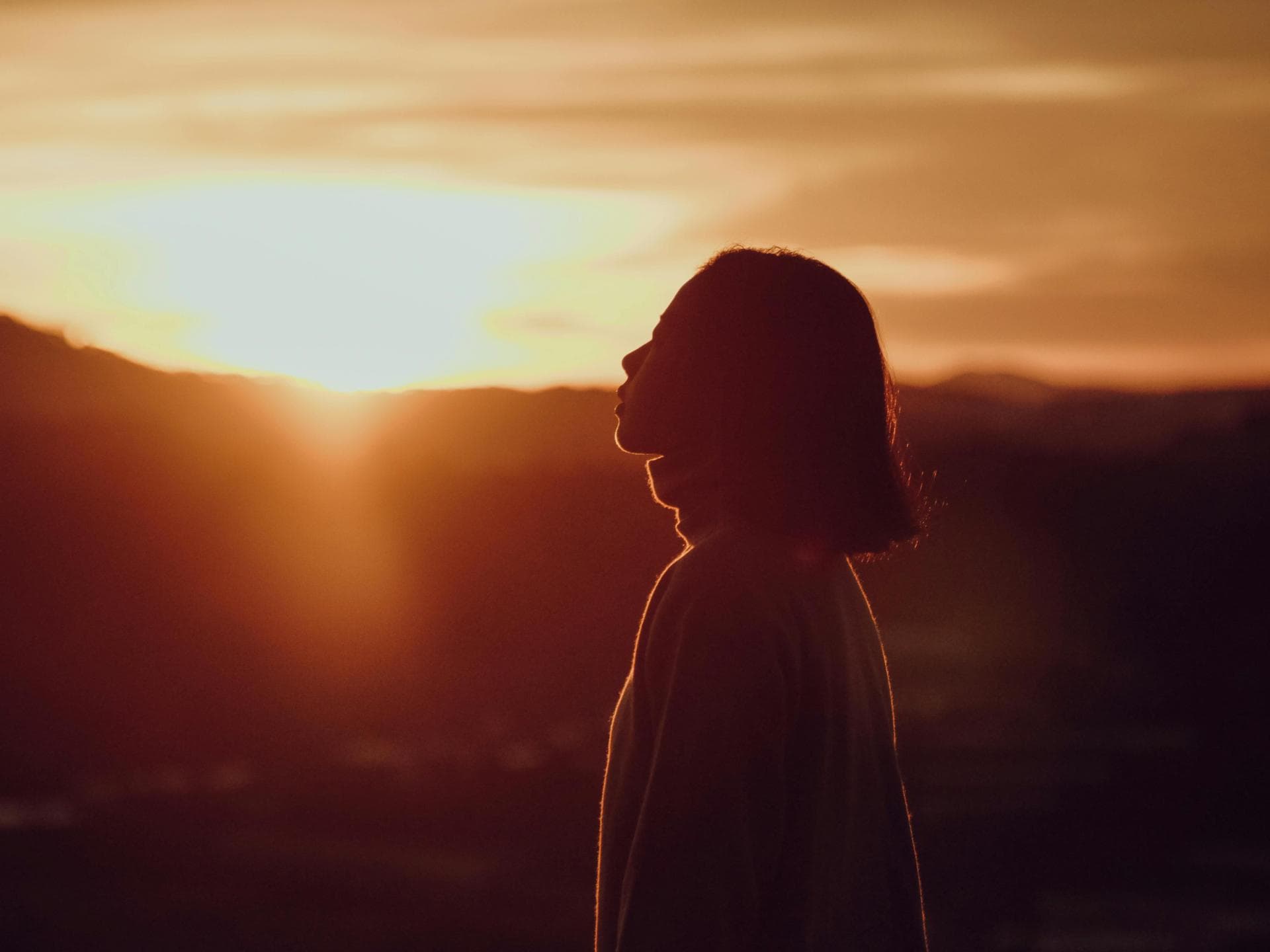 Pech-Sternzeichen am Wochenende Frau mit kurzen Haaren steht vor einem Sonnenuntergang