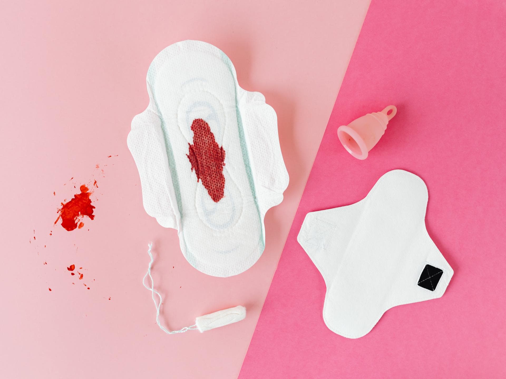 Periode Binden, Tampon und Menstruationstasse liegen auf einem rosafarbenen Hintergrund