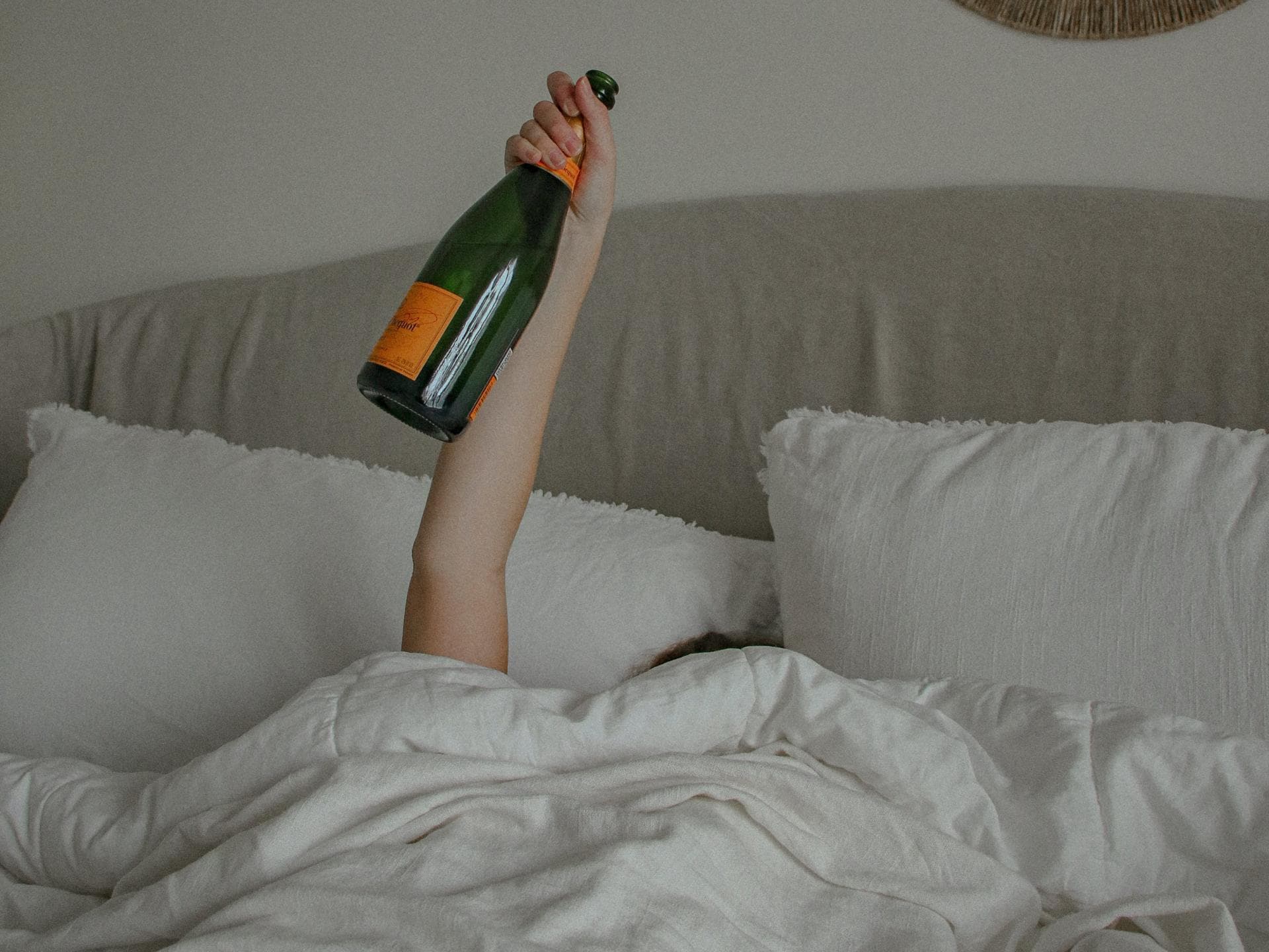 Frau im Bett hält mit einem Arm eine Flasche Alkohol in die Luft