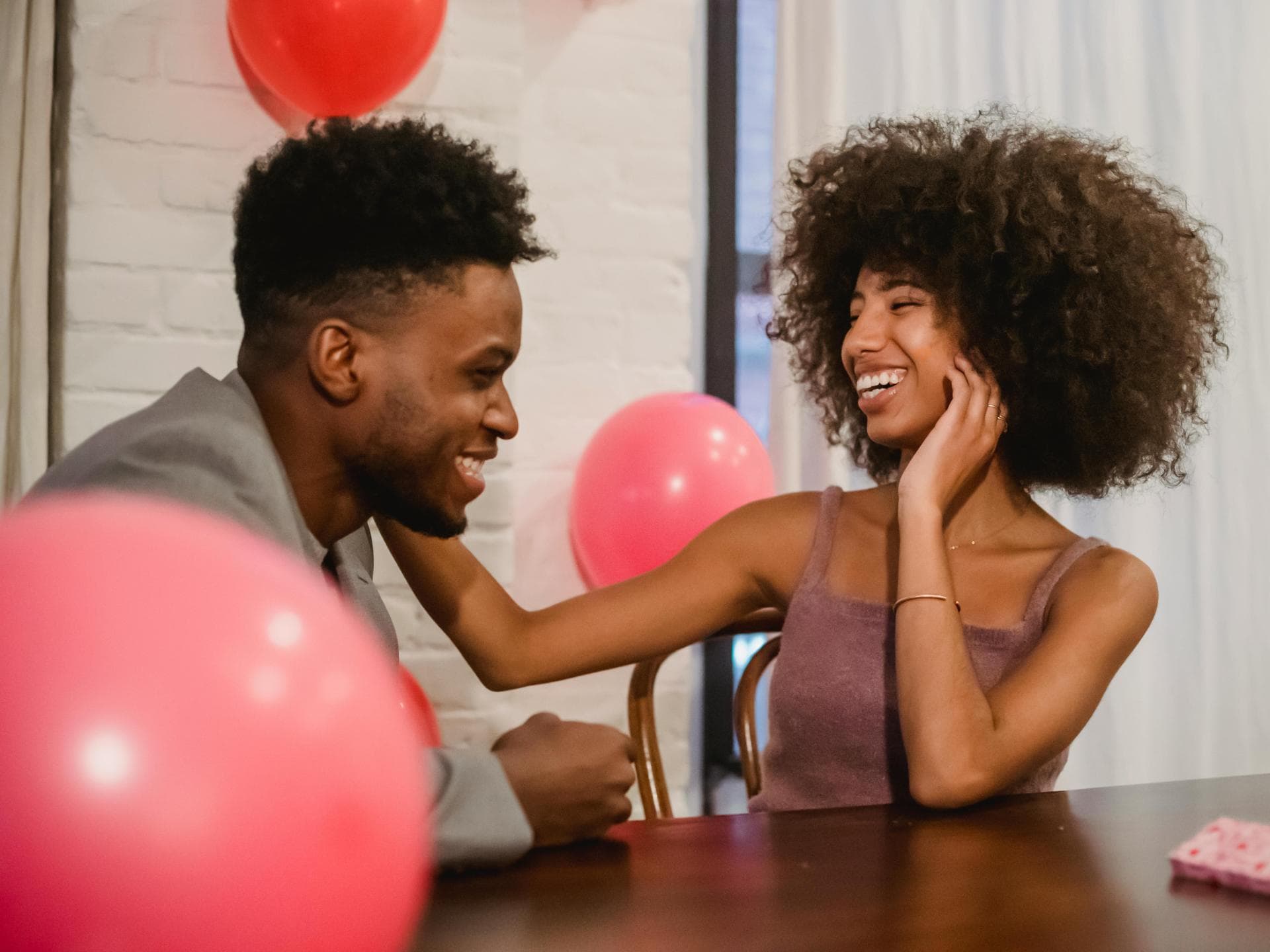Mann und Frau sitzen am Tisch mit Luftballons und lachen