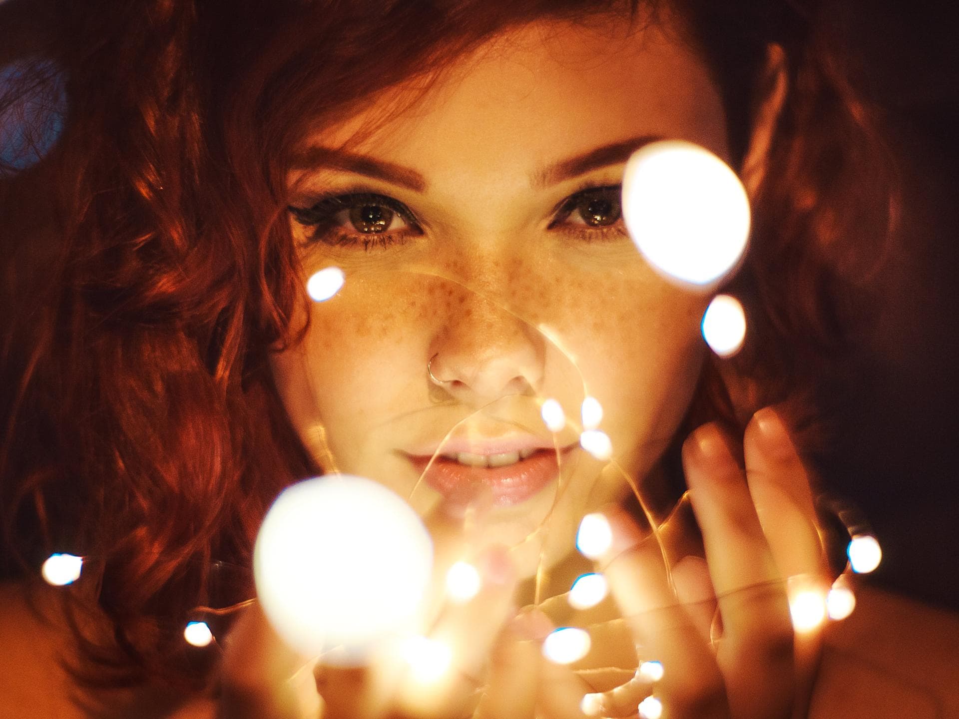 Wochenhoroskop Januar Frau mit Sommersprossen und Eyeliner hält eine Lichterkette in der Hand