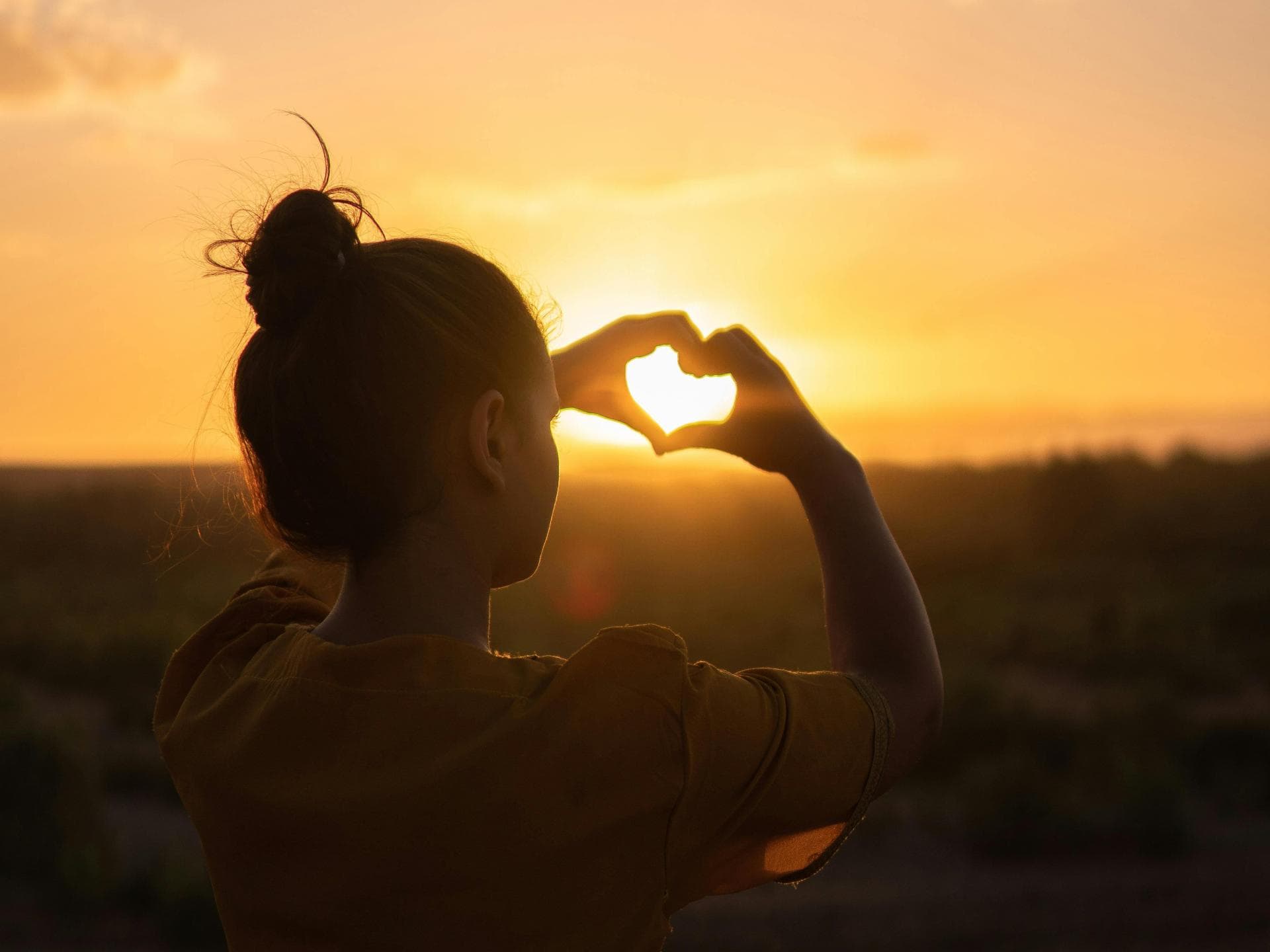 Sternzeichen, die heimlich verliebt sind Frau macht Herz mit Händen vor Sonnenuntergang