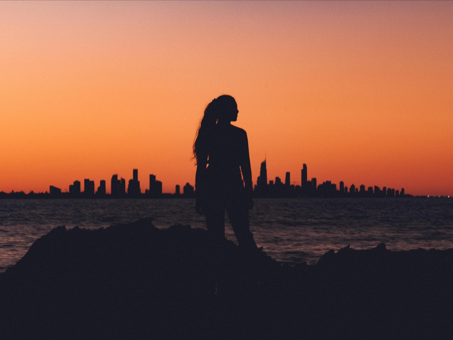 Frau steht vor einer Skyline während des Sonnenuntergangs
