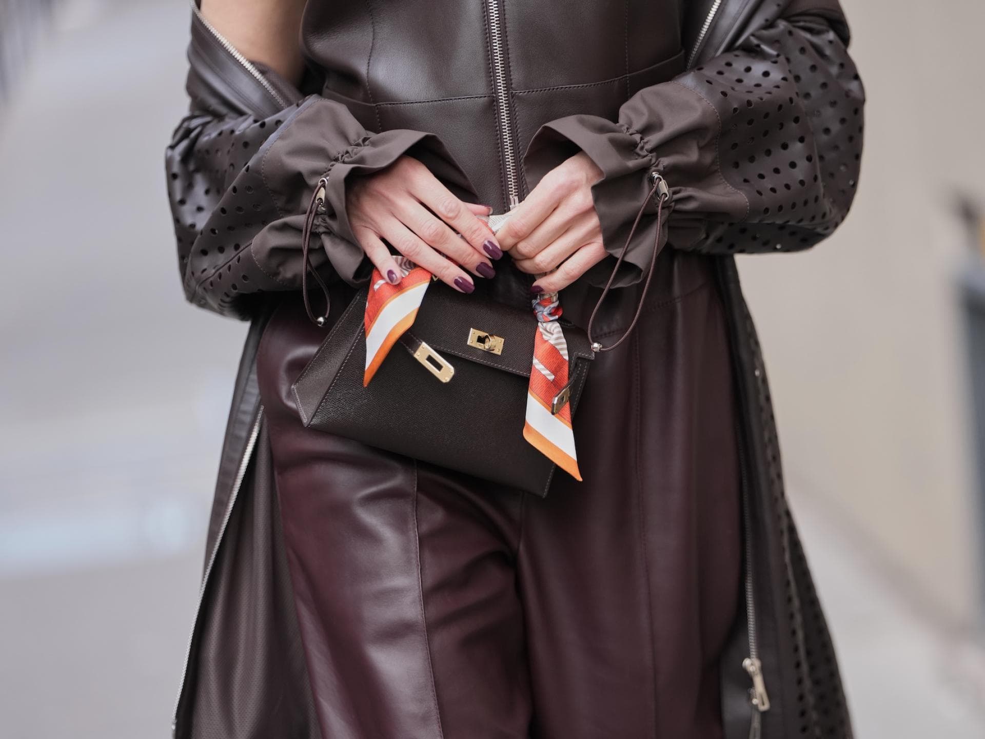 Braune Fingernägel sind besonders im Trend, wenn sie kurz sind. Eine Frau trägt ein braunes Outfit und hält vorn ihre Tasche mit den Fingern fest.