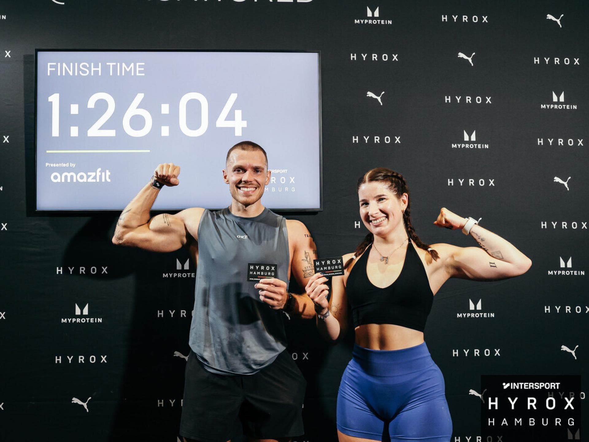 Redakteurin Laura und ihr Freund haben den Hyrox geschafft und sind stolz. Eine Frau und ein Mann mit Hyrox Patches vor ihrer Finish-Zeit.