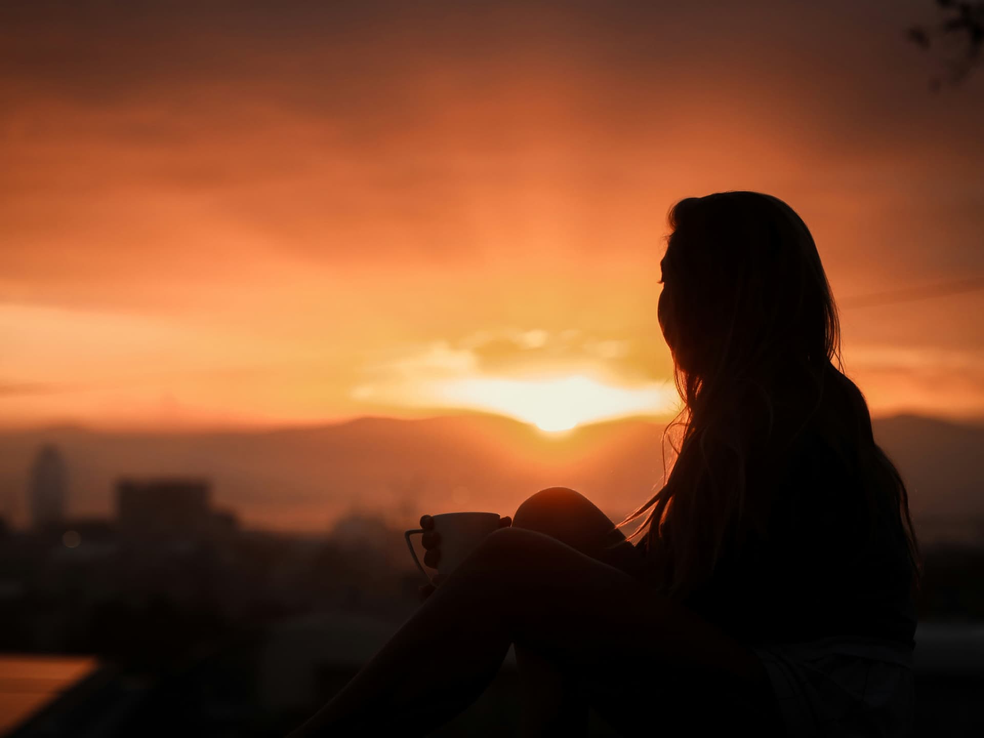 Frau sitzt vor Abendhimmel