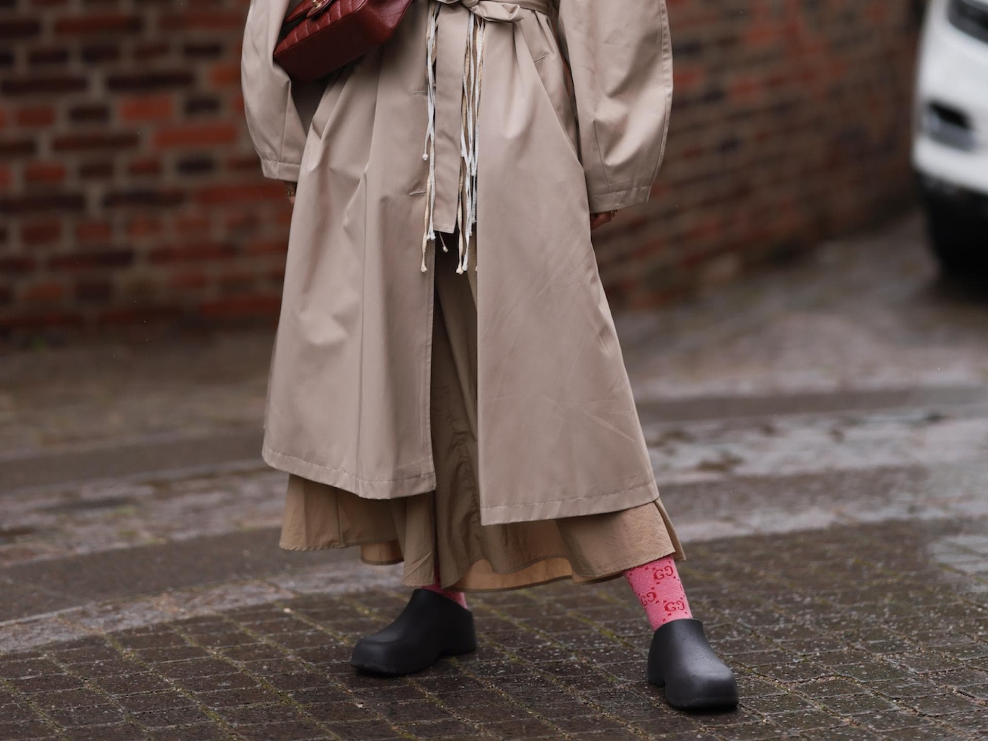 Frau im beigen Mantel mit Garden Shoes und einer weinroten Tasche.
