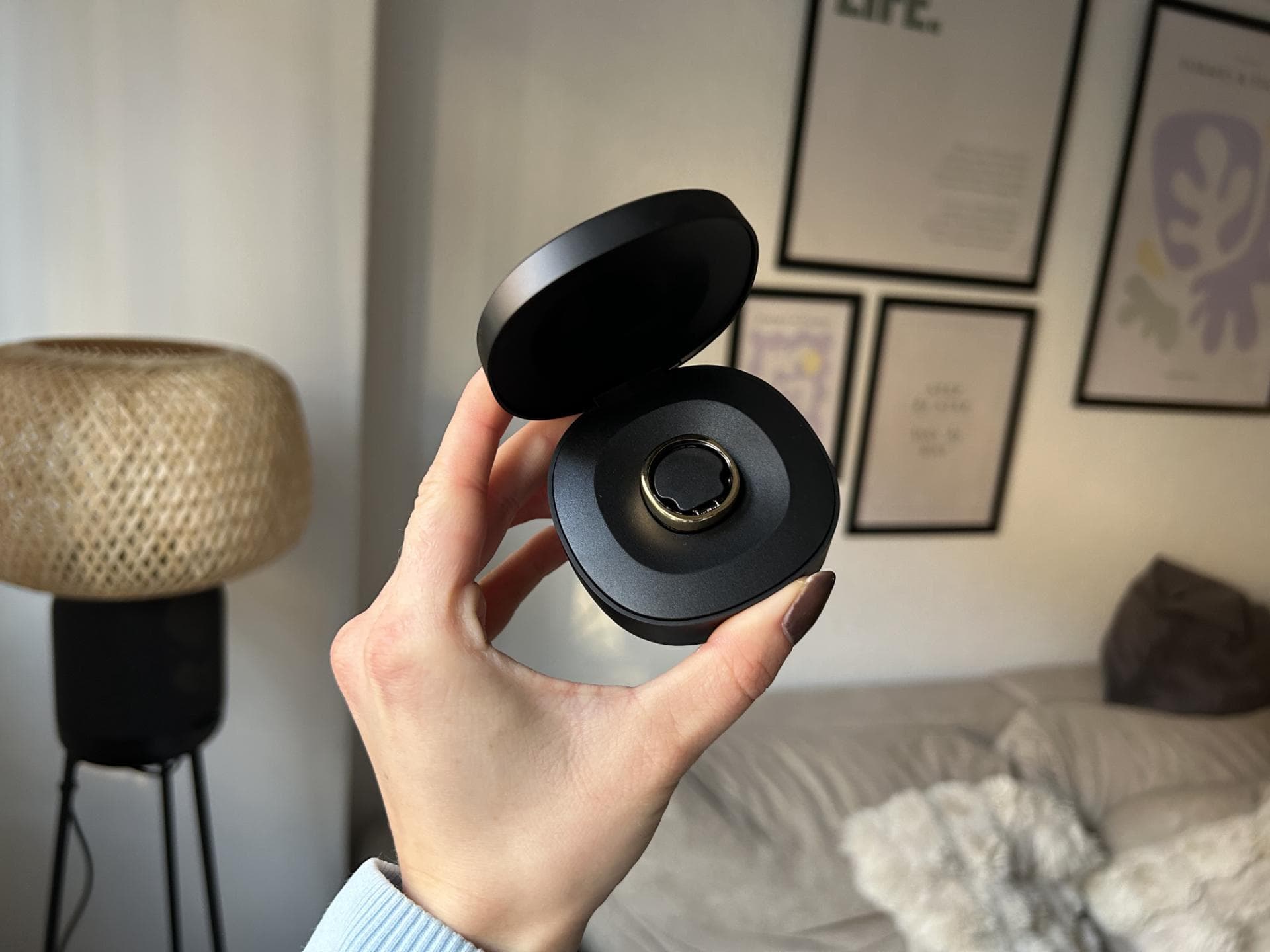 Der Smart Ring lässt sich bequem in einer Box aufladen. Ein goldener Ring in einer schwarzen Ladebox wird in der Hand gehalten.