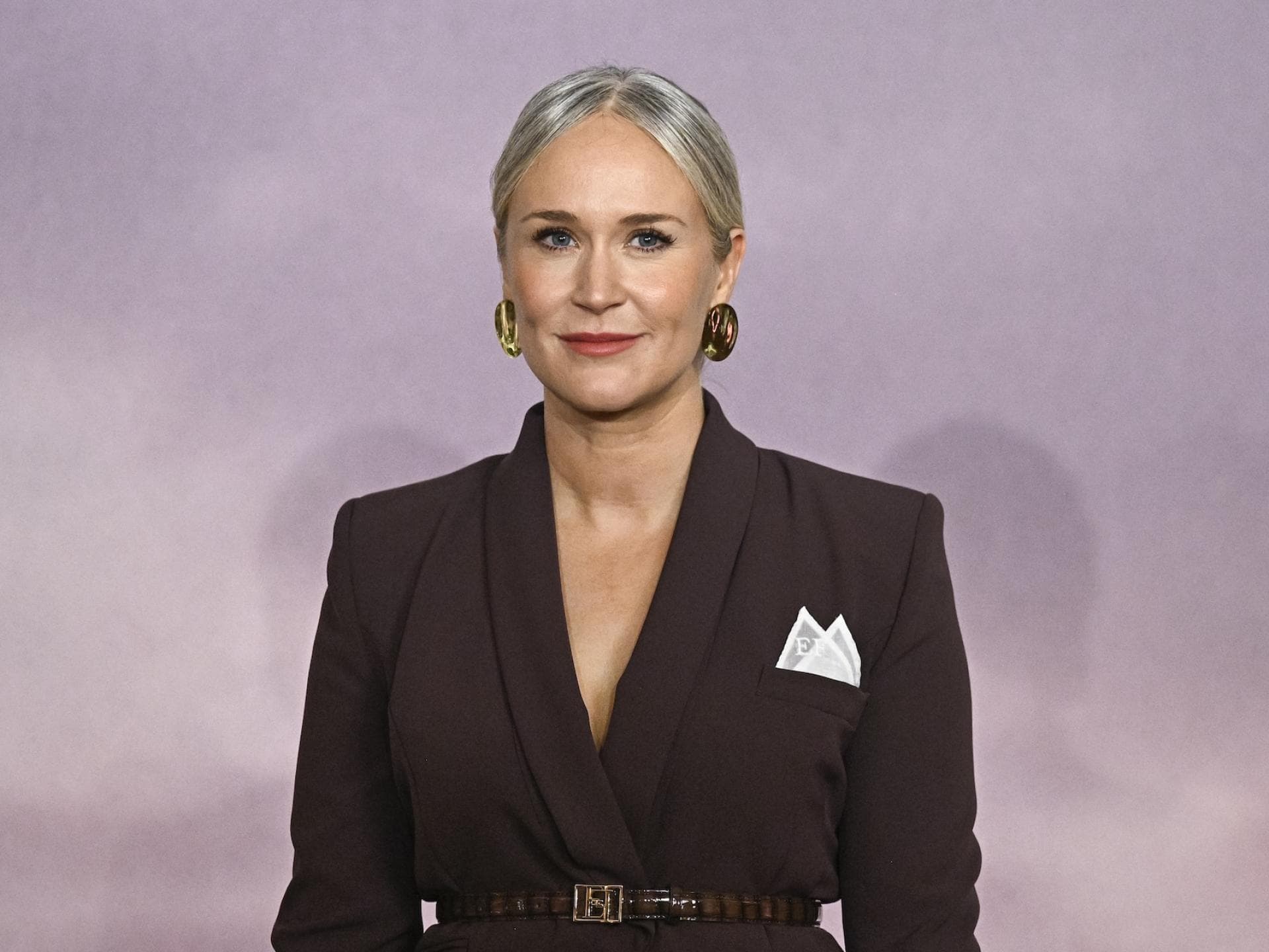 Jess Brownell mit einem dunklen Hosenanzug und zwei Einstecktüchern mit den Buchstaben „E“ und „F“.