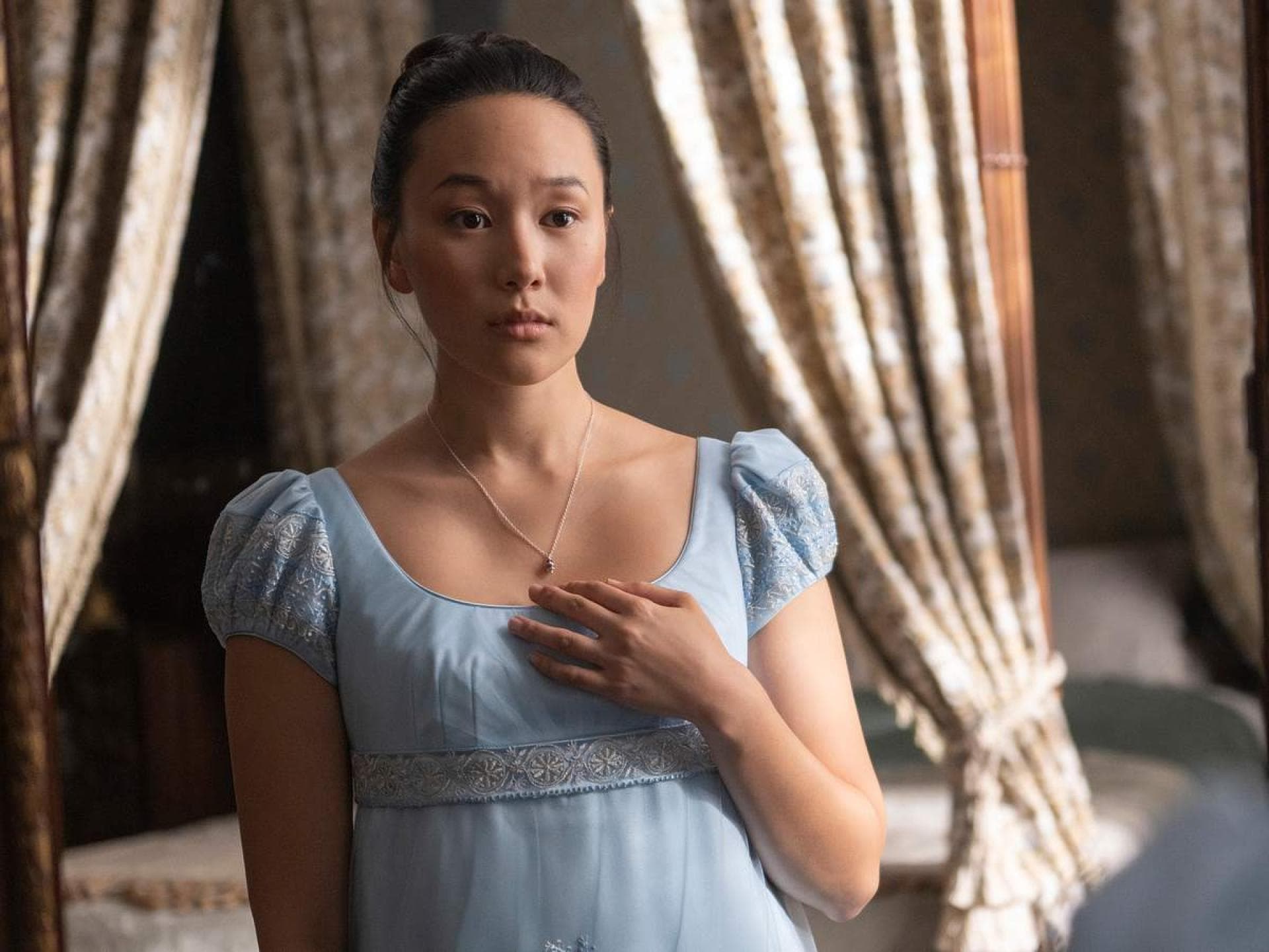 Sophie spielt die Hauptrolle in der vierten Staffel von „Bridgerton“. Eine junge Frau in einem babyblauen Kleid guckt starr nach vorn und fasst sich an ihr Dekollete.