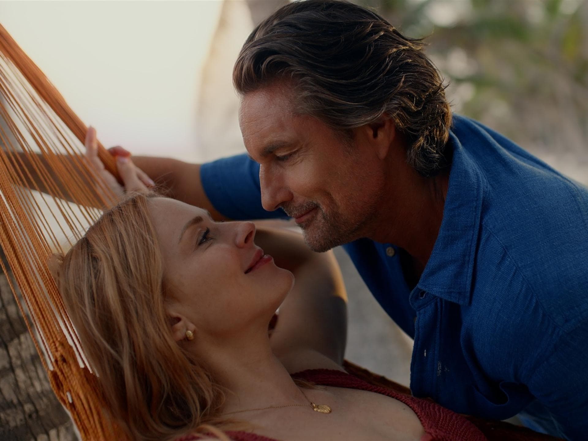 Eine Frau auf einer Hängematte lächelt einen Mann an, der über sie gebeugt ist.