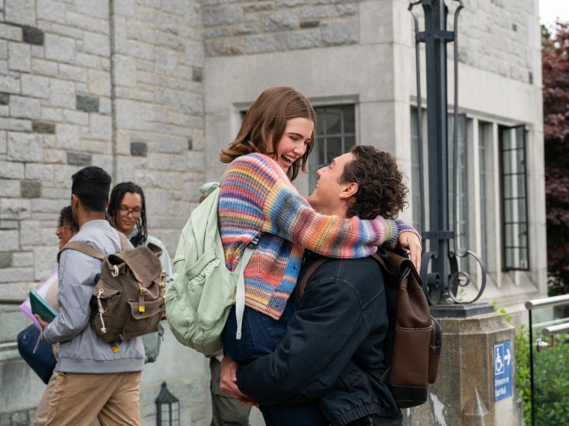 Ella Bright und Belmont Cameli spielen die Hauptrollen in der Serie „Off Campus“. Eine junge Frau mit einem bunt gestreiften Cardigan wird von einem Mann hochgehoben.