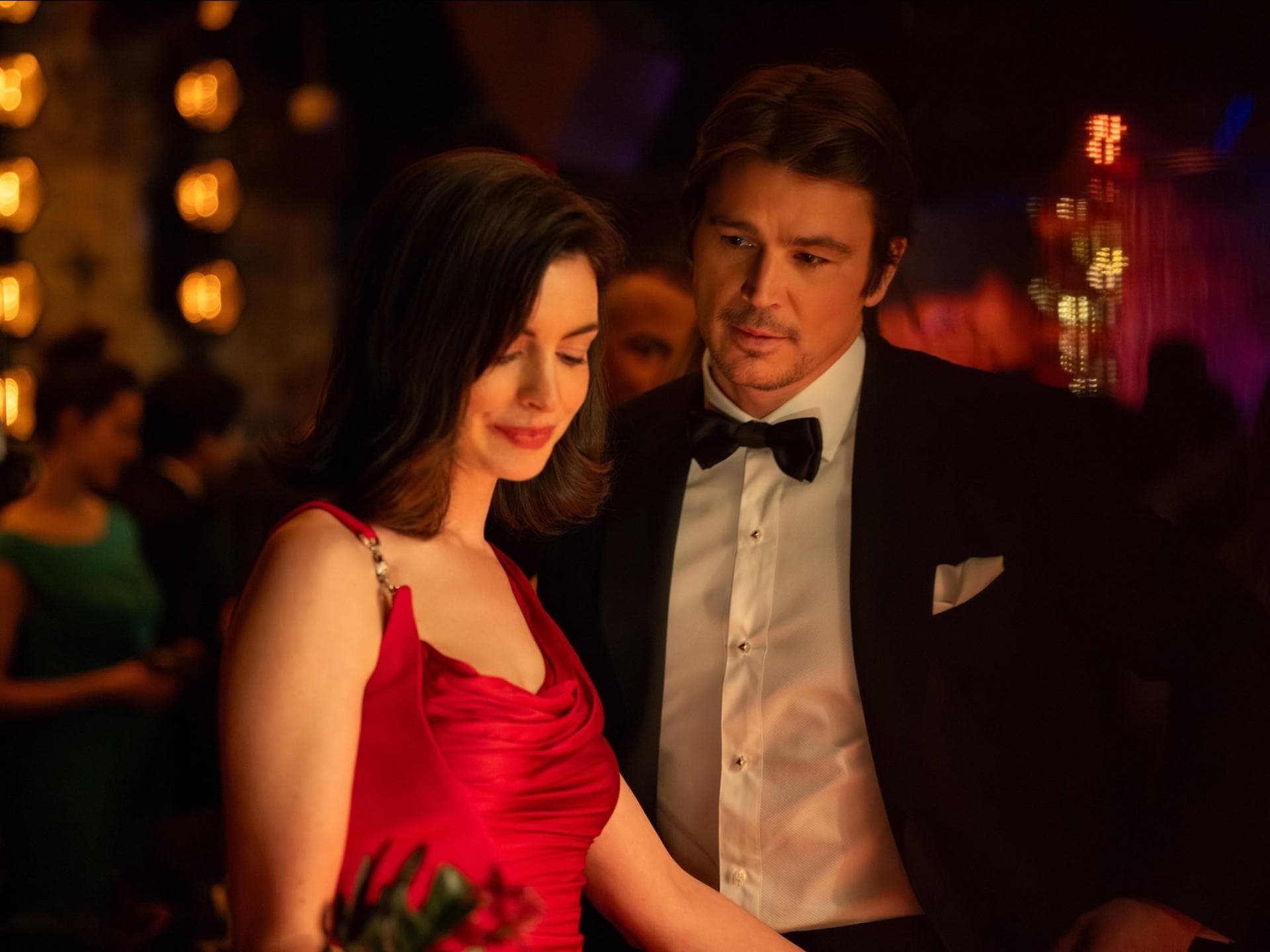 Anne Hathaway steht in einem roten Kleid und schaut nach unten, Josh Hartnett steht hinter ihr und schaut sie an.