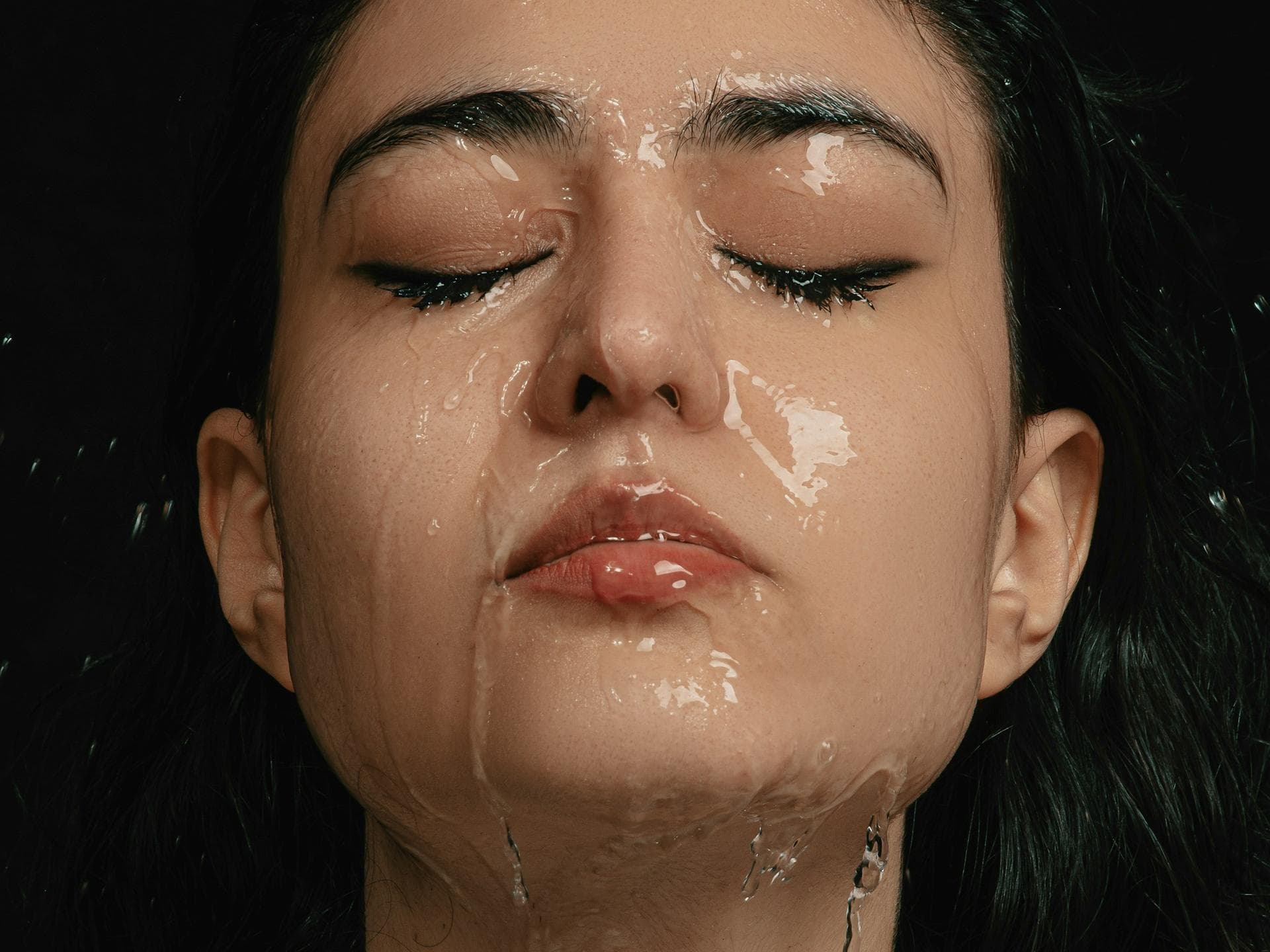 Einer Frau mit geschlossenen Augen läuft Wasser über das komplette Gesicht.