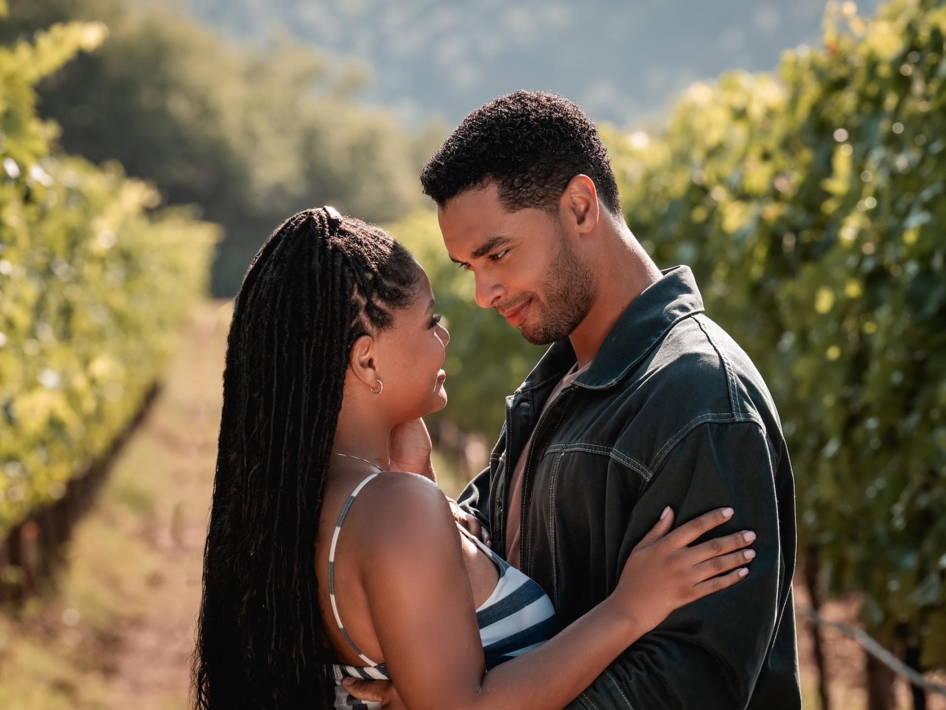 Anna (Halle Bailey) und Michael (Regé-Jean Page) sind die Hauptrollen in „YOU, ME & ITALY“. Eine Frau mit langen dunklen Haaren und ein Mann mit dunklen Haaren stehen auf einem Weinberg und schauen sich innig an.