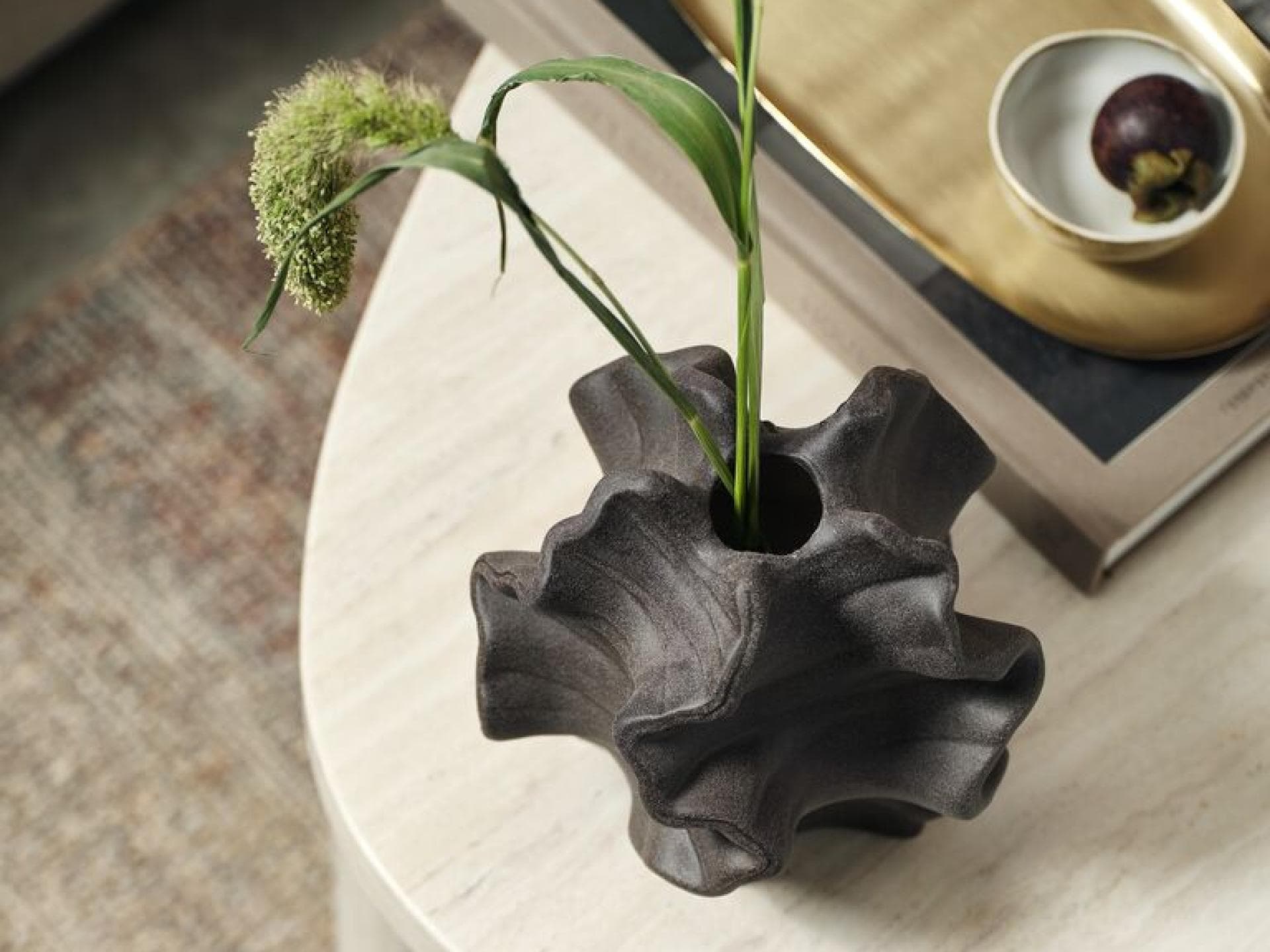 Bei Jysk kann man tolle Deko-Pieces preiswert kaufen. Eine organische Vase mit ein paar Gräsern auf einem Couchtisch von oben betrachtet.