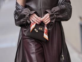 Eine Frau trägt ein braunes Outfit und hält vorn ihre Tasche mit den Fingern fest.