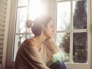 Frau schaut traurig aus dem Fenster