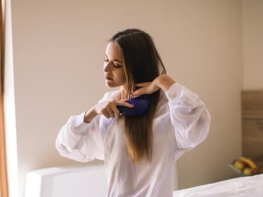 Haare kämmen: Frau sitzt auf einem Bett und bürstet die Haare