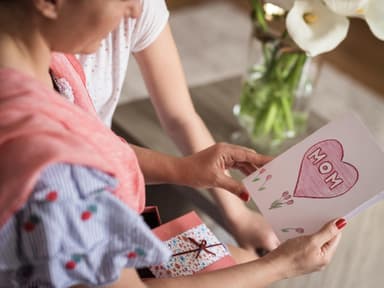 Muttertagssprüche: Frau hält eine Karte in der Hand auf der "Mom" steht