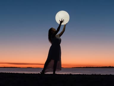 Horoskop: Frau hält einen Vollmond in der Hand am Strand