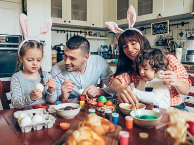 Warum feiern wir Ostern? Familie sitzt am Tisch und bemalt Ostereier