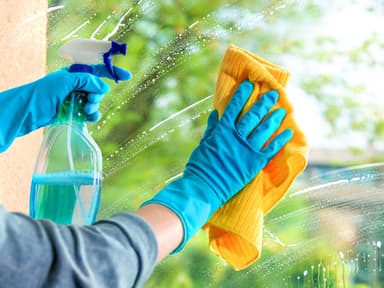 Fenster putzen: Hände mit Putzhandschuhen säubern eine Fensterscheibe