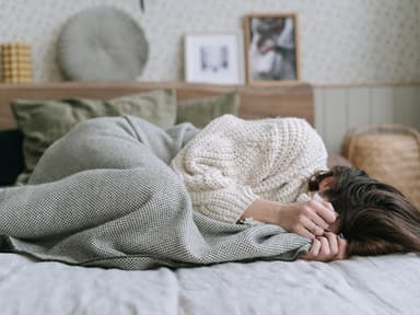 Frau im Bett mit Händen vor Gesicht 