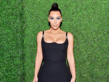 Kim Kardashian im schwarzen Kleid vor grüner Wand