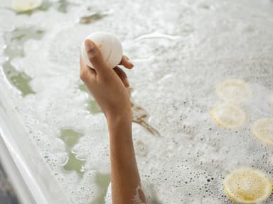 Badekugel in Hand und Badewanne