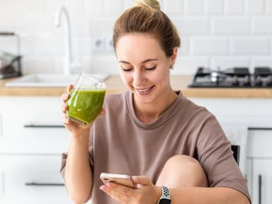 Frau mit grünem Saft schaut auf Handy