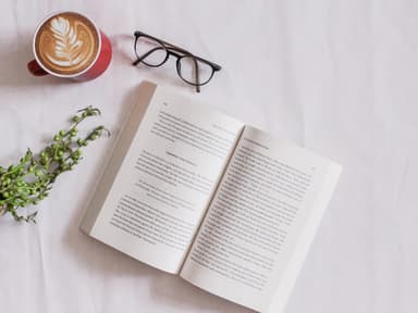 Buch liegt neben Brille und Kaffee