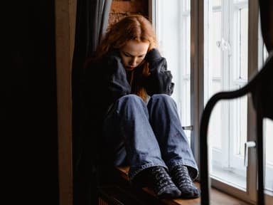 Traurige Frau sitzt auf einer Fensterbank