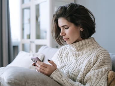 Frau mit kurzen braunen Haaren schaut traurig auf ihr Smartphone