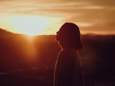 Frau mit kurzen Haaren steht vor einem Sonnenuntergang