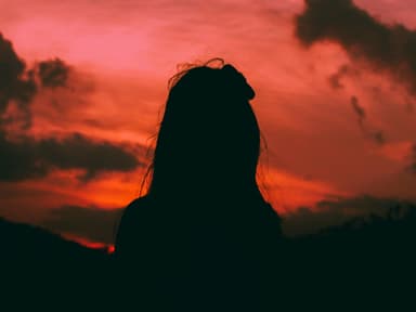 Silhouette einer Frau mit langen Haaren vor einem orange-rosafarbenen Himmel