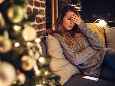Gestresste Frau sitzt auf dem Sofa, neben ihr ein geschmückter Tannenbaum