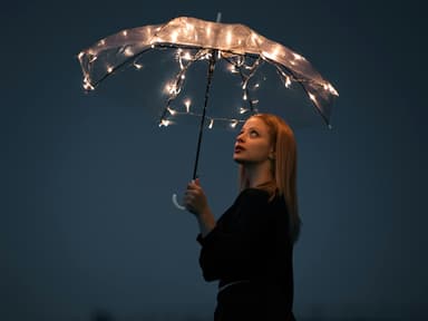Frau hält einen Regenschirm mit Lichterketten in der Hand