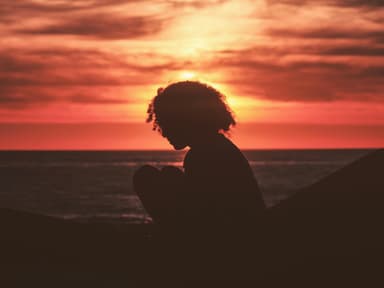 Frau sitzt beim Sonnenuntergang am Meer